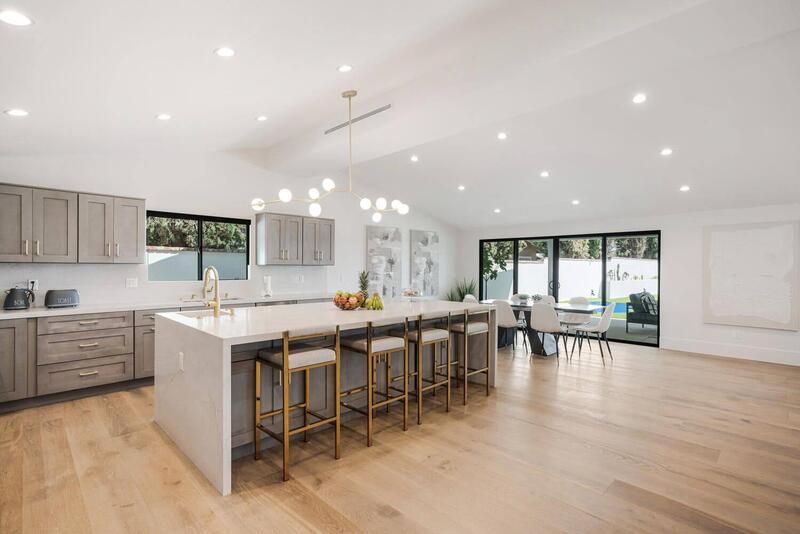 Modern kitchen with island and seating, wood floors, light cabinets, and dining area.