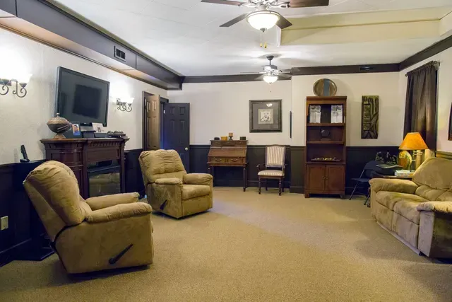 Spacious living room with beige carpet, sofas, armchairs, a lamp, and a ceiling fan.