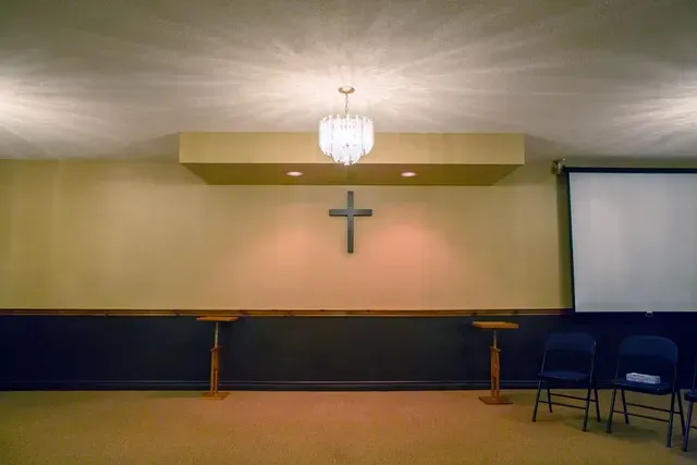 Empty church stage with a cross, chandelier, and two blue chairs