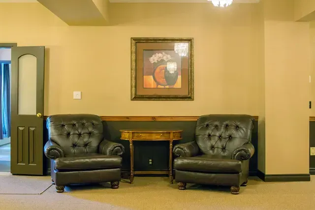 Lobby seating area with two black tufted chairs, a small table, and framed artwork on beige walls