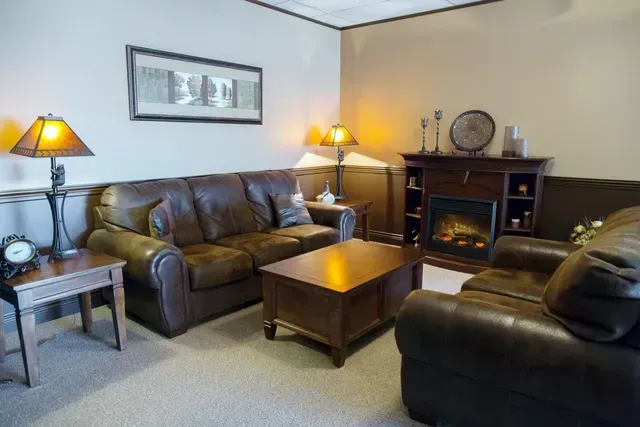 Cozy living room with brown leather sofas, lamps, coffee table, fireplace, and framed wall art
