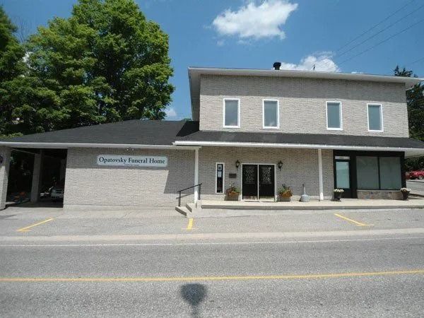 Small gray commercial building with a storefront sign and parking lot on a sunny street