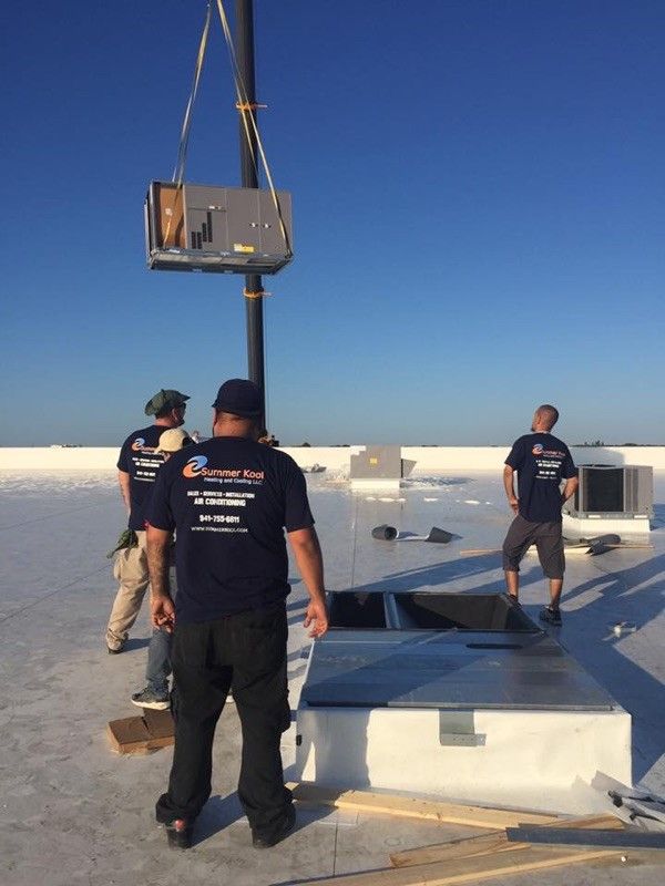 HVAC workers on a rooftop, lifting a unit with a crane, against a blue sky