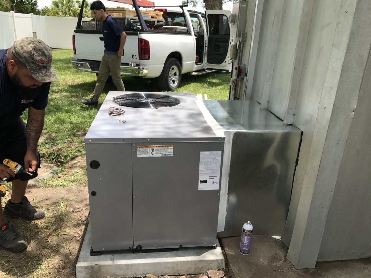 Two men installing a new air conditioning unit next to a building, in a yard