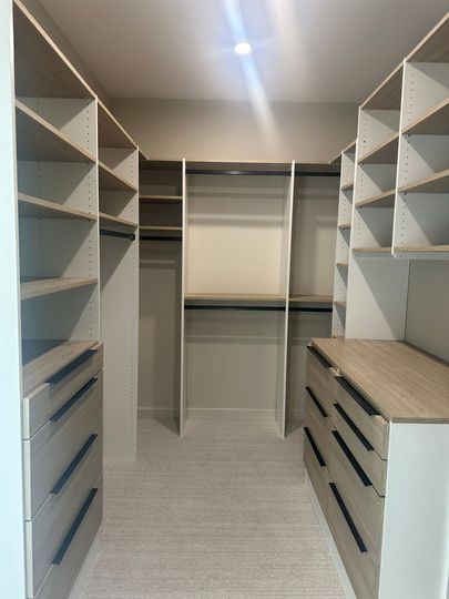 Walk-in closet with white shelves and drawers on both sides, carpeted floor, and hanging rods at the back.