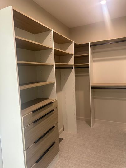 Empty walk-in closet with white shelving, hanging rod, and built-in drawers on the left.