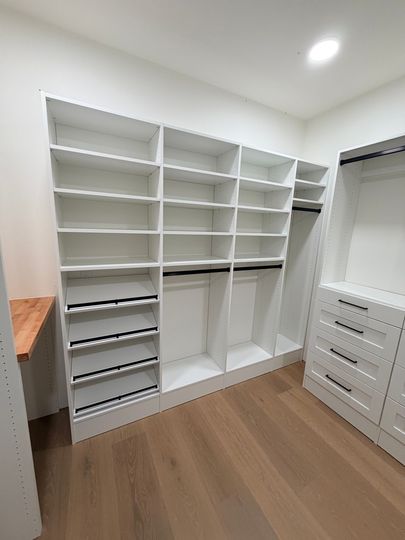 Walk-in closet with white shelving, drawers, and hanging space on a wood floor.