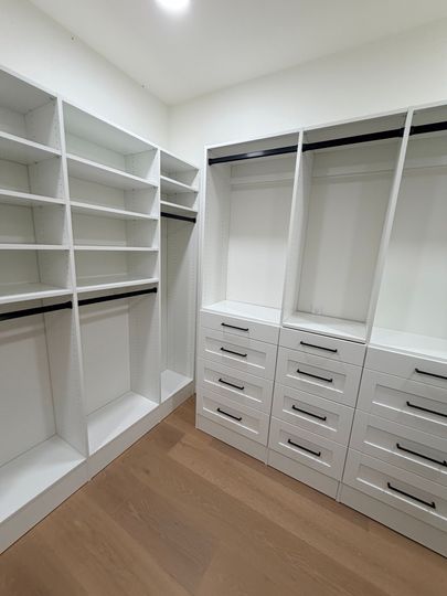 Walk-in closet with white shelves, hanging rods, drawers, and wood flooring