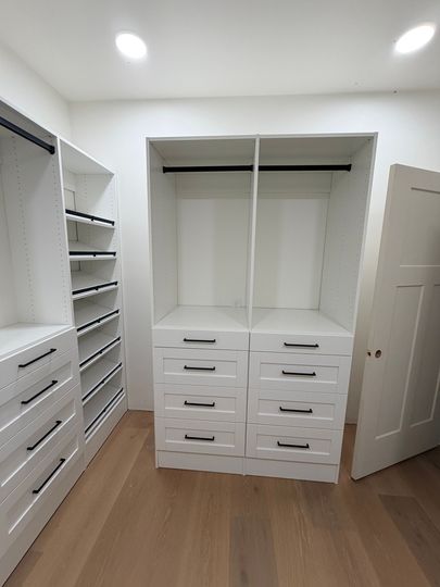 Walk-in closet with white shelving and drawers, open door, and wood flooring