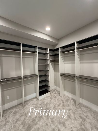 Walk-in closet with white shelving, hanging rods, and gray carpet under a ceiling light.