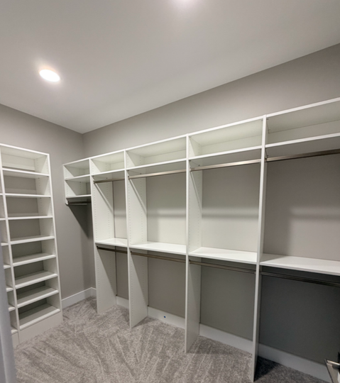 Empty walk-in closet with white shelving, hanging rods, and gray carpeted floor