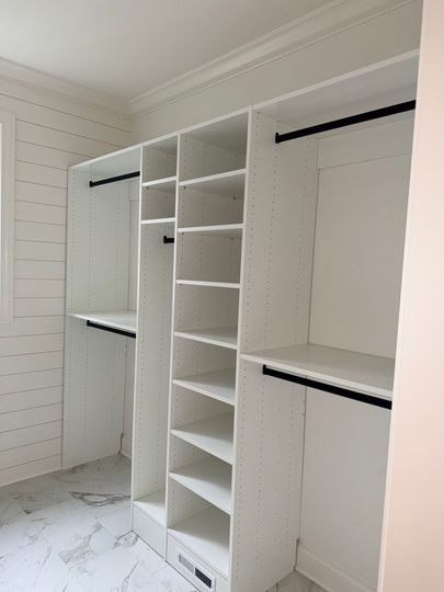 Walk-in closet with white built-in shelving, hanging rods, and marble-look tile floor.