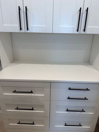 White built-in cabinets and drawers with black handles in a recessed storage nook.