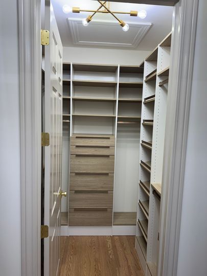 Built-in white closet with shelves, drawers, and hanging rods, viewed down a hallway with wood floor.