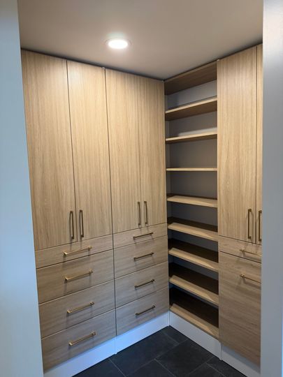 Walk-in closet with light wood cabinets, shelves, and drawers under a ceiling light.