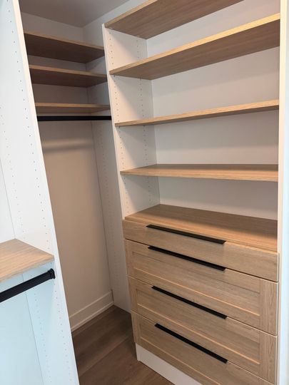 Walk-in closet with white shelves, hanging rod, and woven drawer units on wood flooring