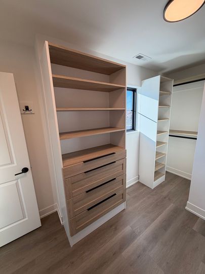 Empty walk-in closet with white shelving, built-in drawers, and wood flooring.