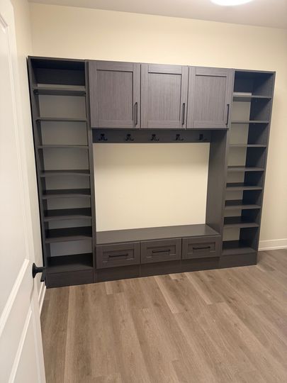 Built-in gray storage wall with shelves, cabinets, and drawers in a carpeted room