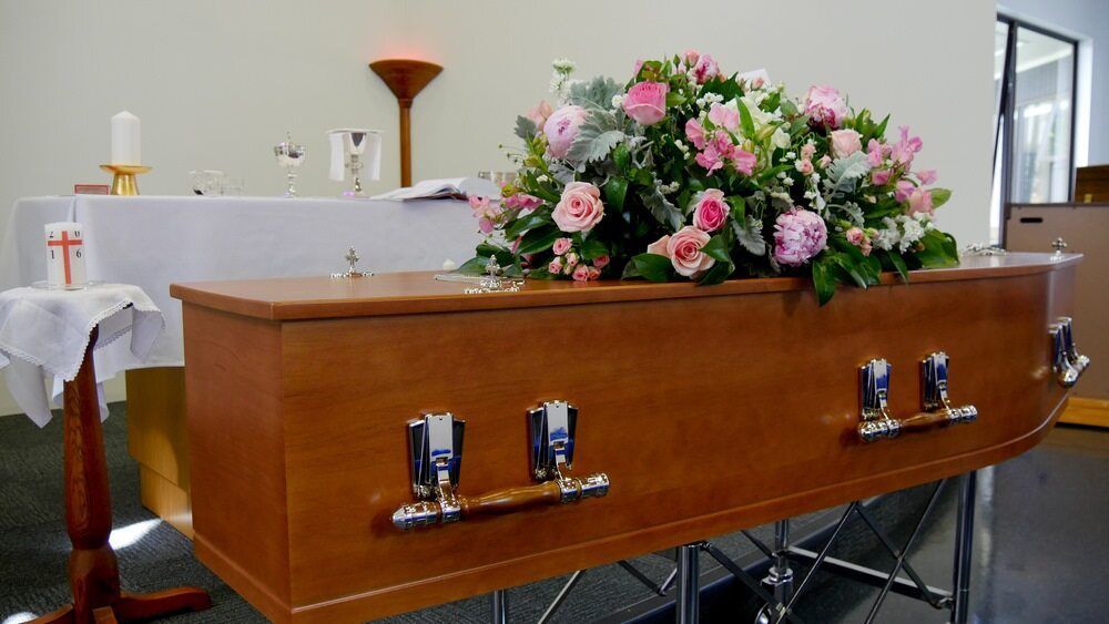 A Wooden Coffin With Flowers on Top of It in a Church — Bull Family Funerals in Warialda, NSW