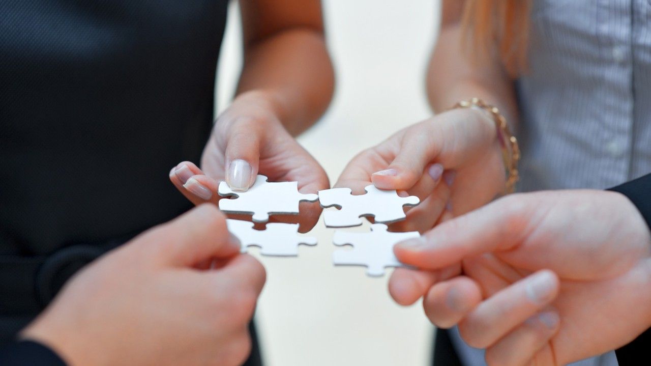 Hands holding white puzzle pieces together over a table in a teamwork activity