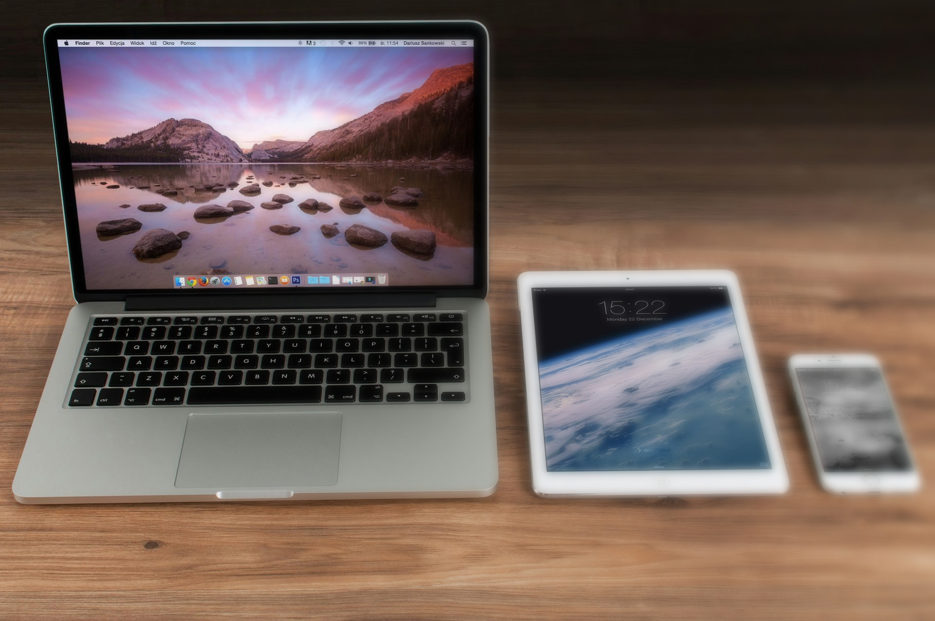 Een laptop, een tablet en een smartphone naast elkaar op een houten oppervlak.