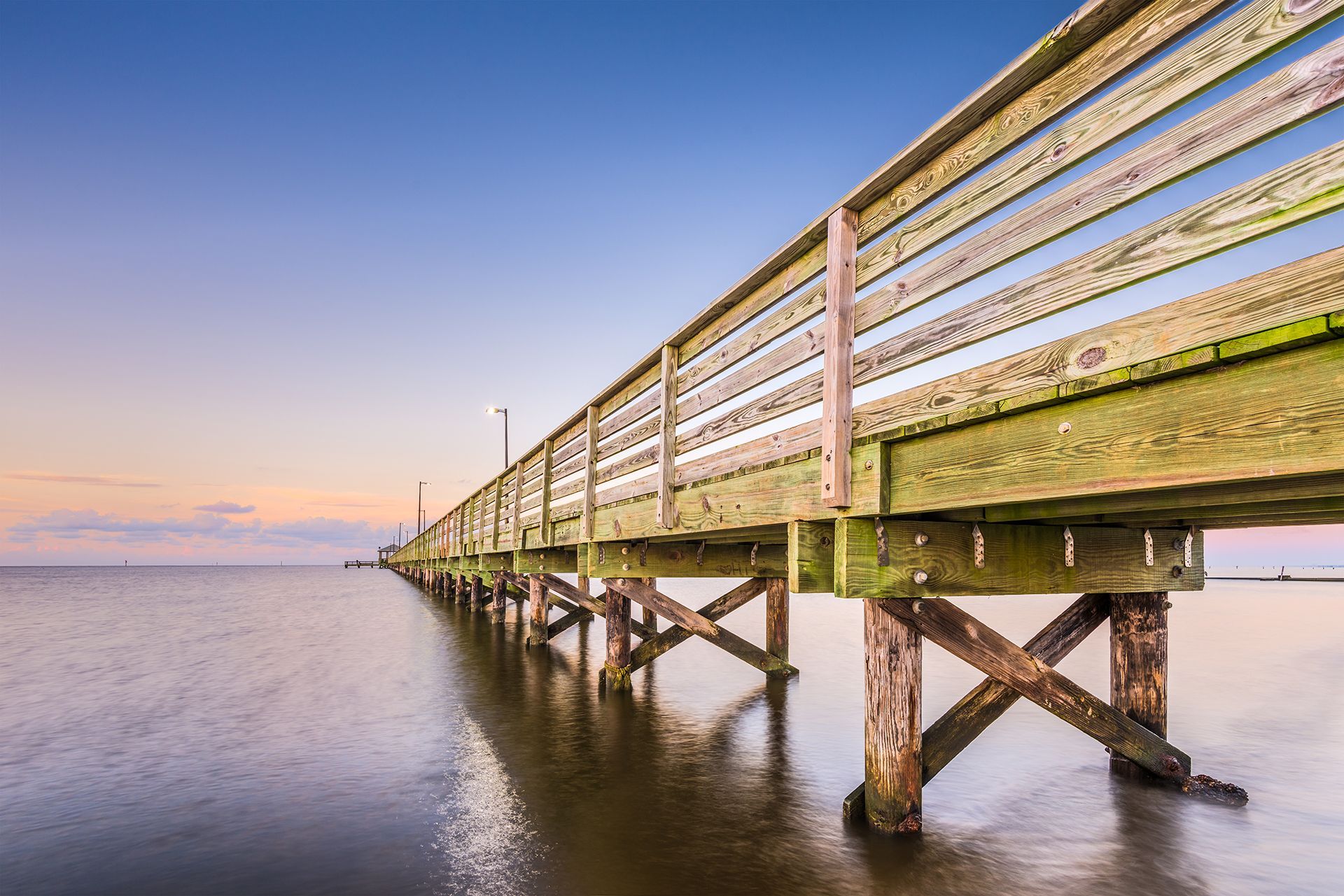 A wooden pier leading into the ocean at sunset.