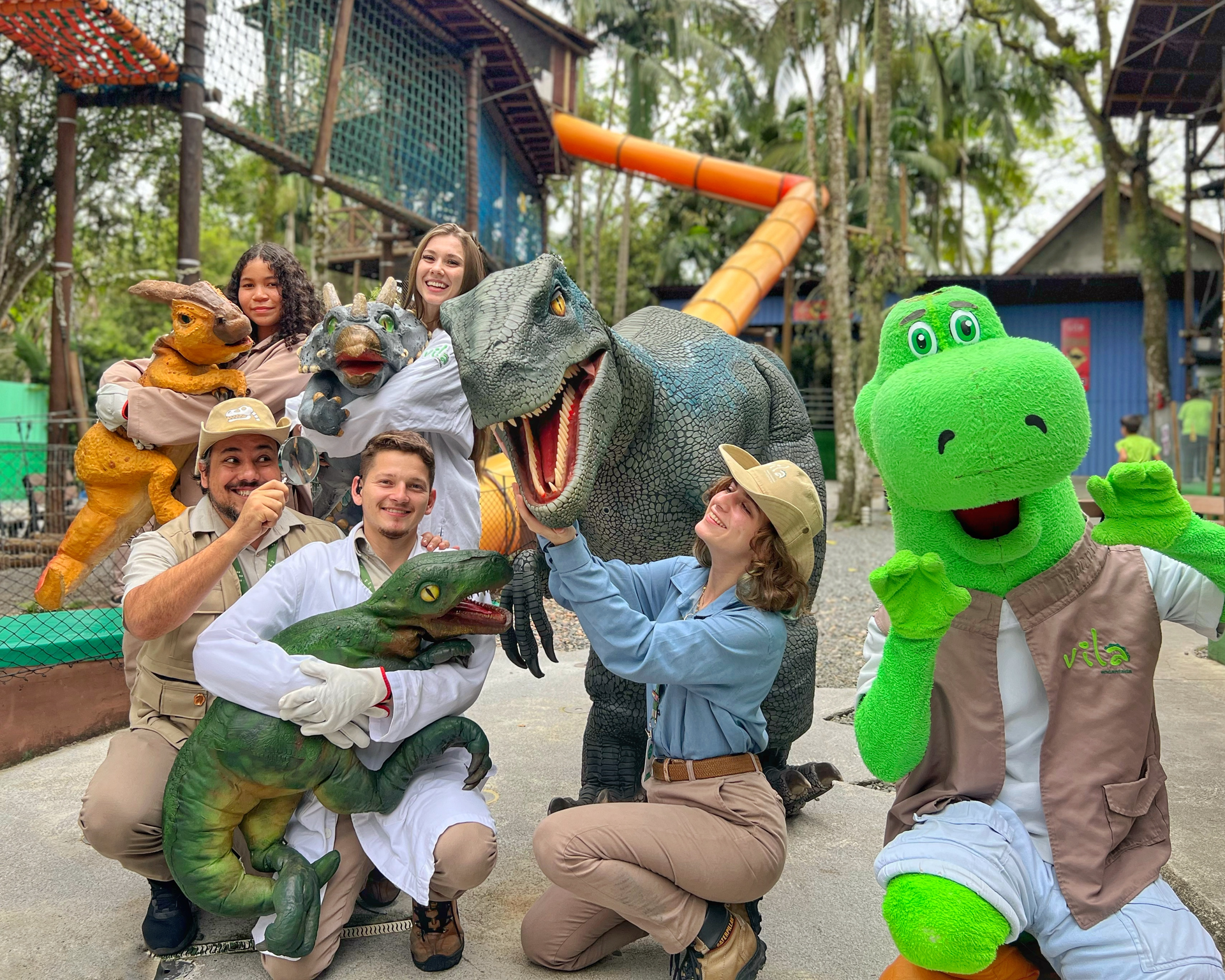 A group of people are posing for a picture with stuffed dinosaurs.