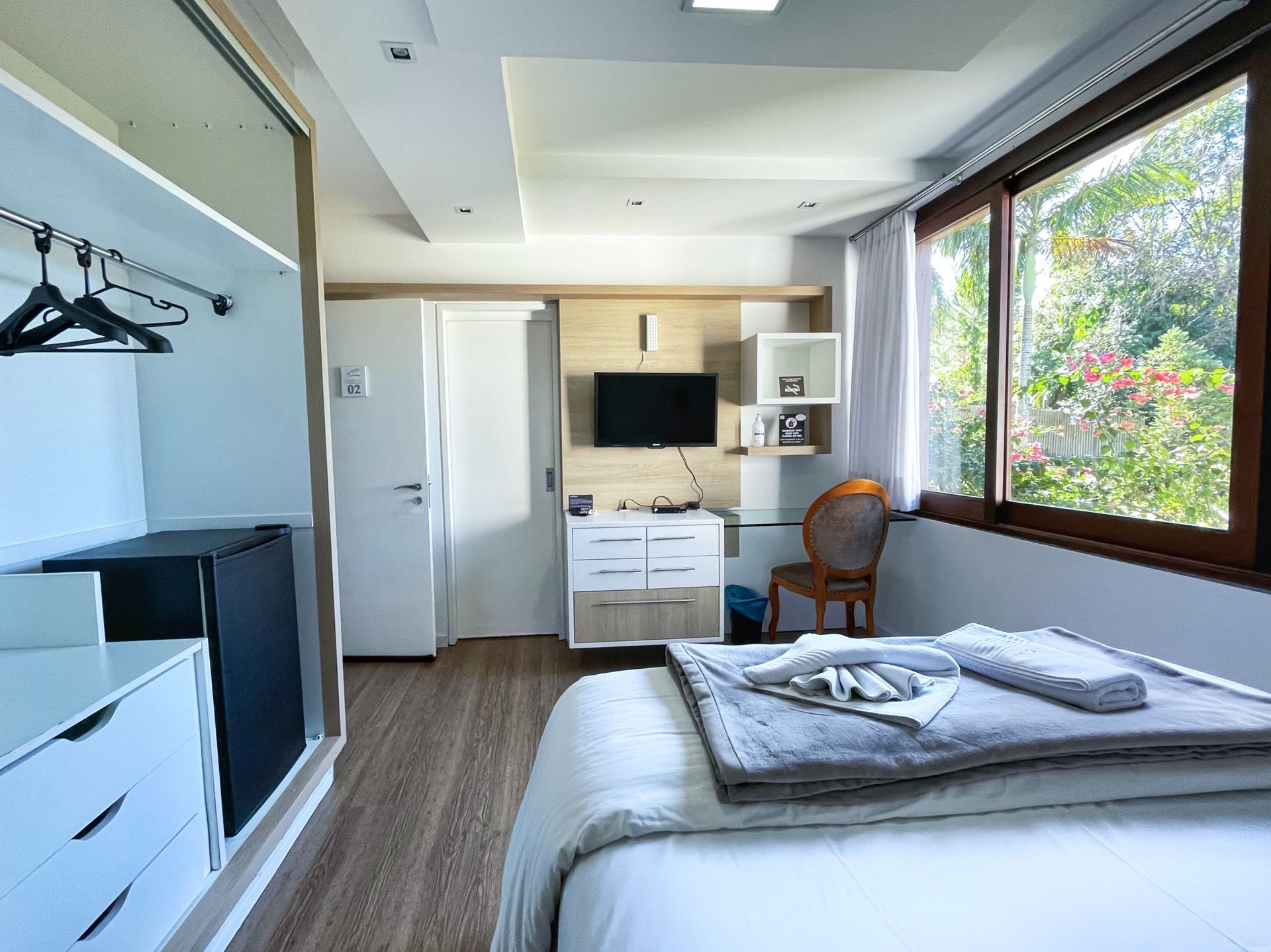 A bedroom with a bed , desk , television and a large window.
