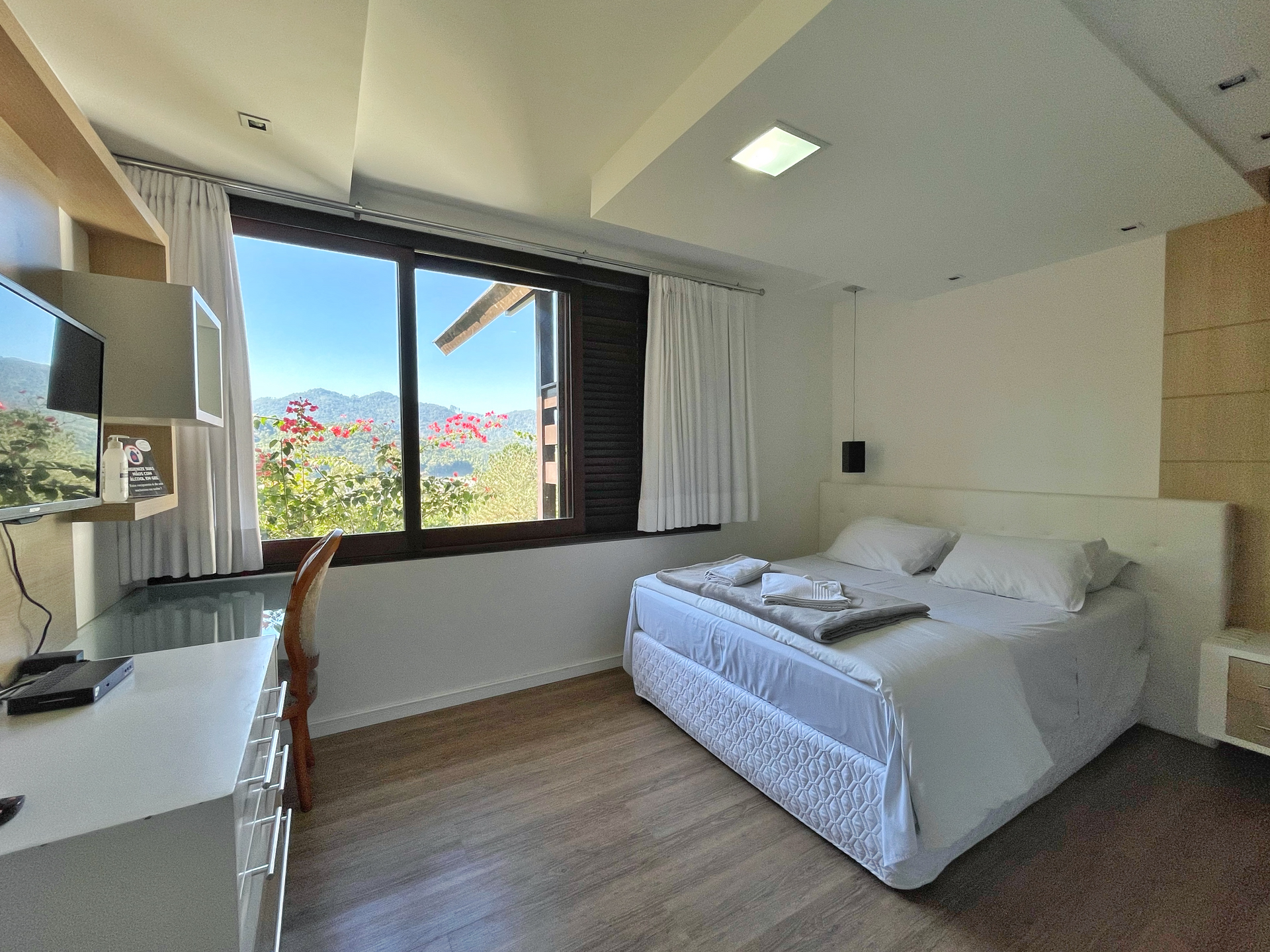 A hotel room with a bed , desk , television and window.
