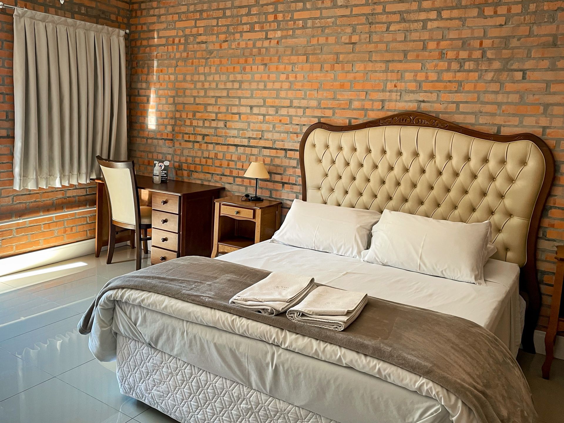 A bedroom with a bed , desk , chairs and a brick wall.