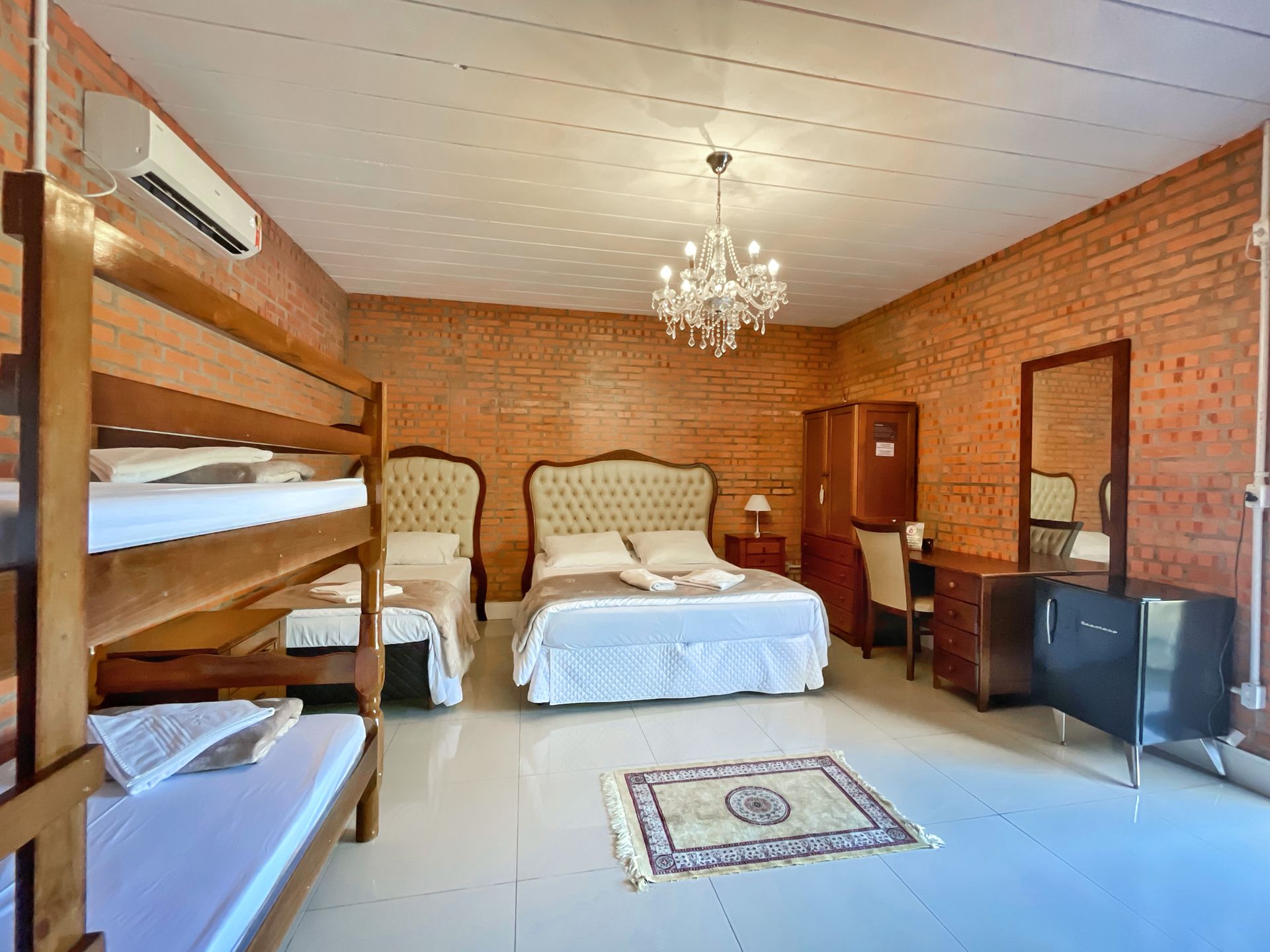 A hotel room with bunk beds , a bed , a desk , a mirror and a chandelier.
