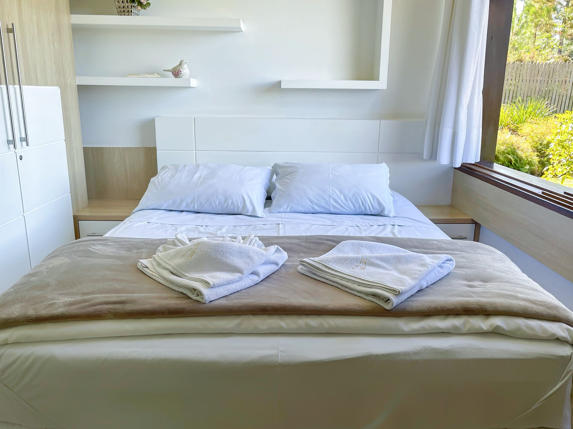 A bed with white sheets and pillows in a bedroom next to a window.