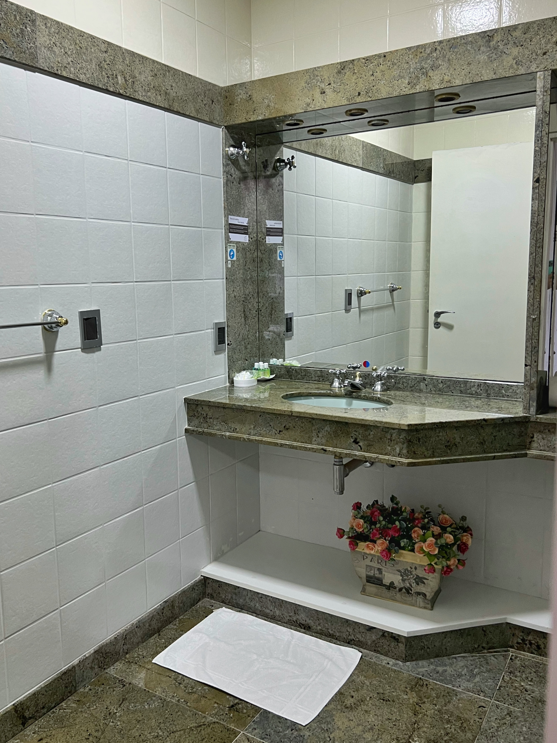 A bathroom with a sink , mirror and a vase of flowers.
