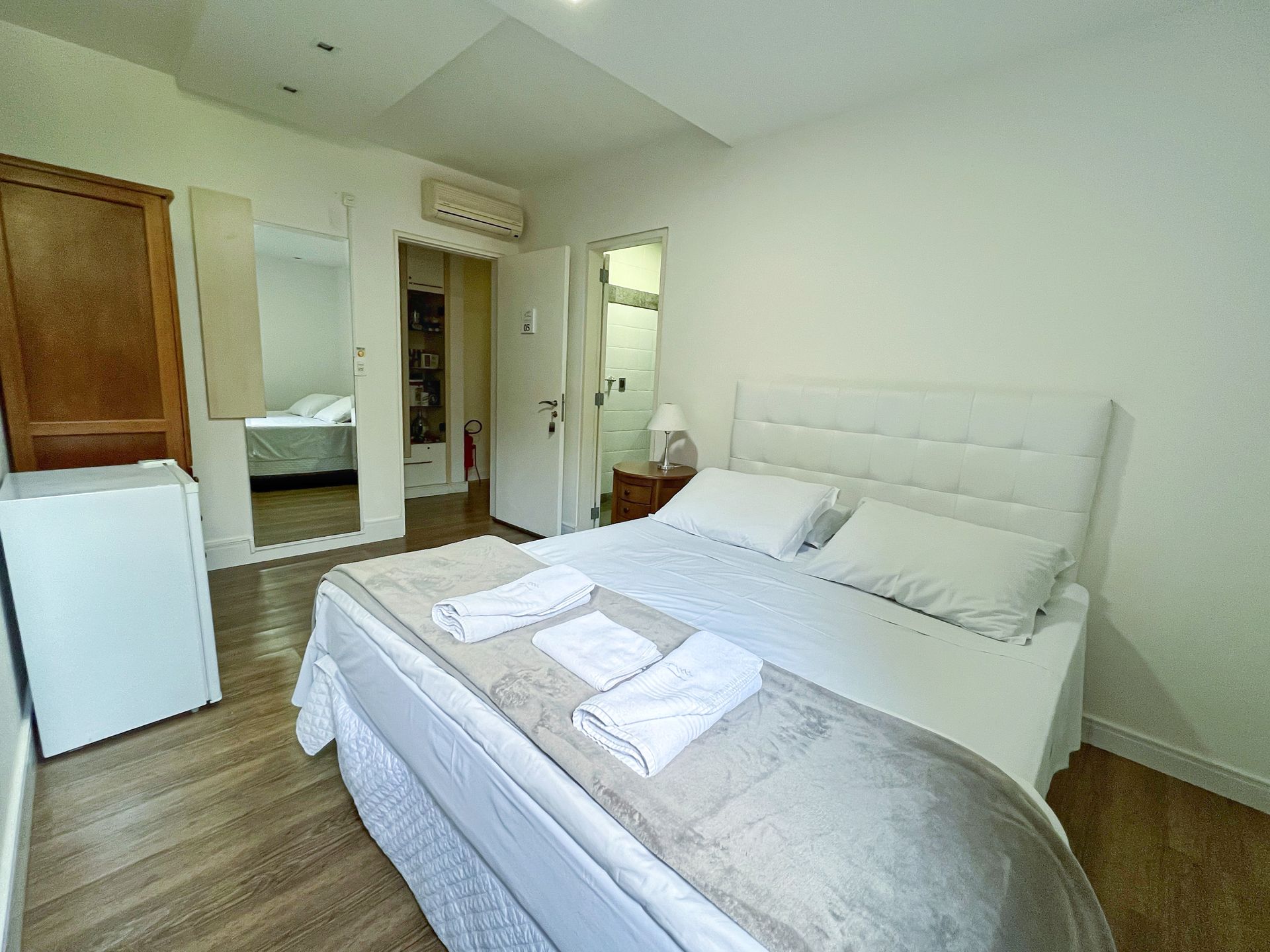 A bedroom with a king size bed and a refrigerator.