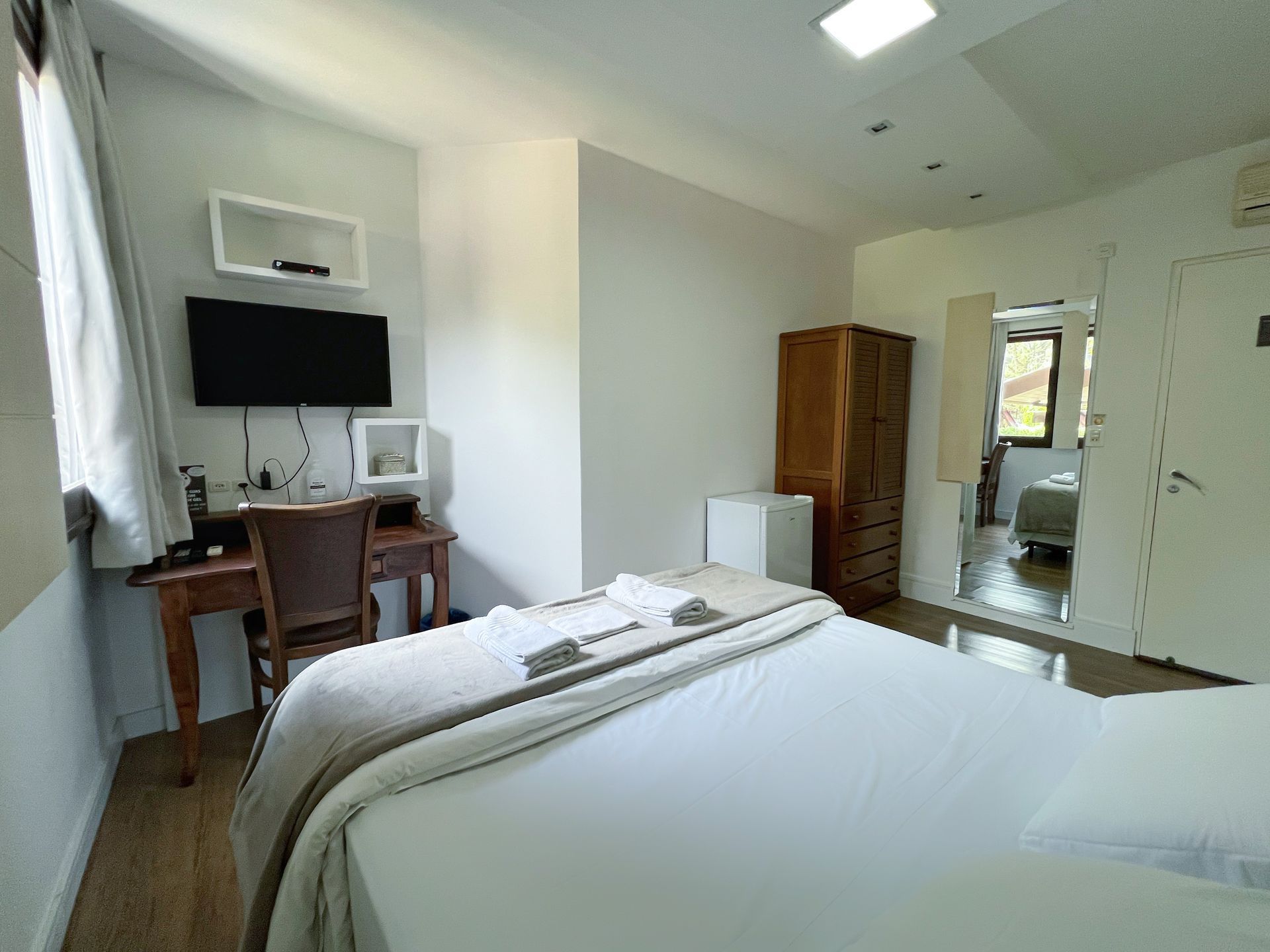 A bedroom with a bed , desk , television and mirror.