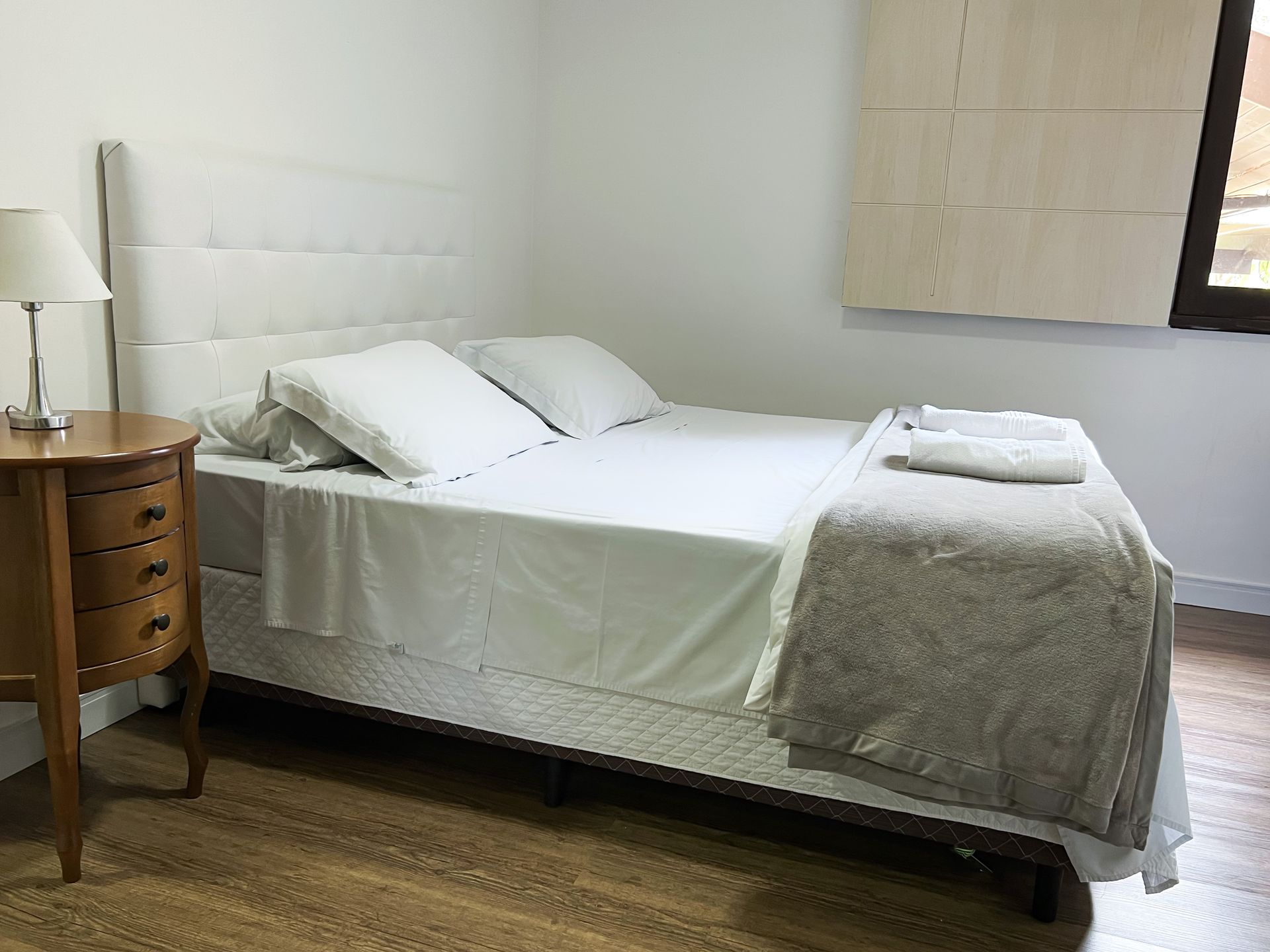 A bedroom with a bed , nightstand , lamp and window.