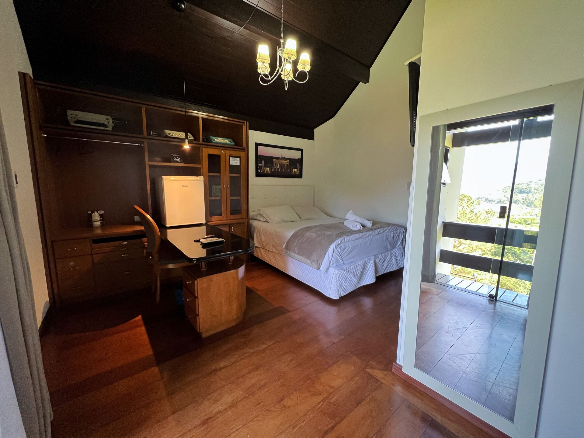 A bedroom with a bed , desk , refrigerator and a balcony.