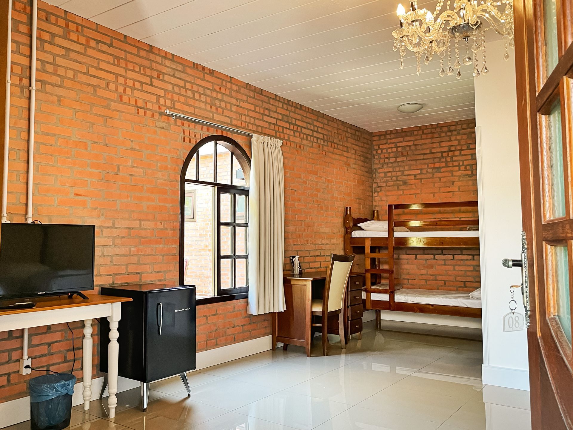 A bedroom with bunk beds , a desk , a television and a chandelier.