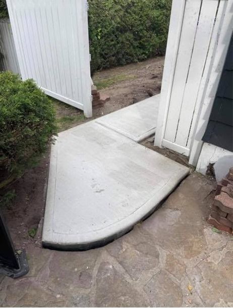 Une passerelle en béton est en cours de construction à côté d'une clôture blanche.