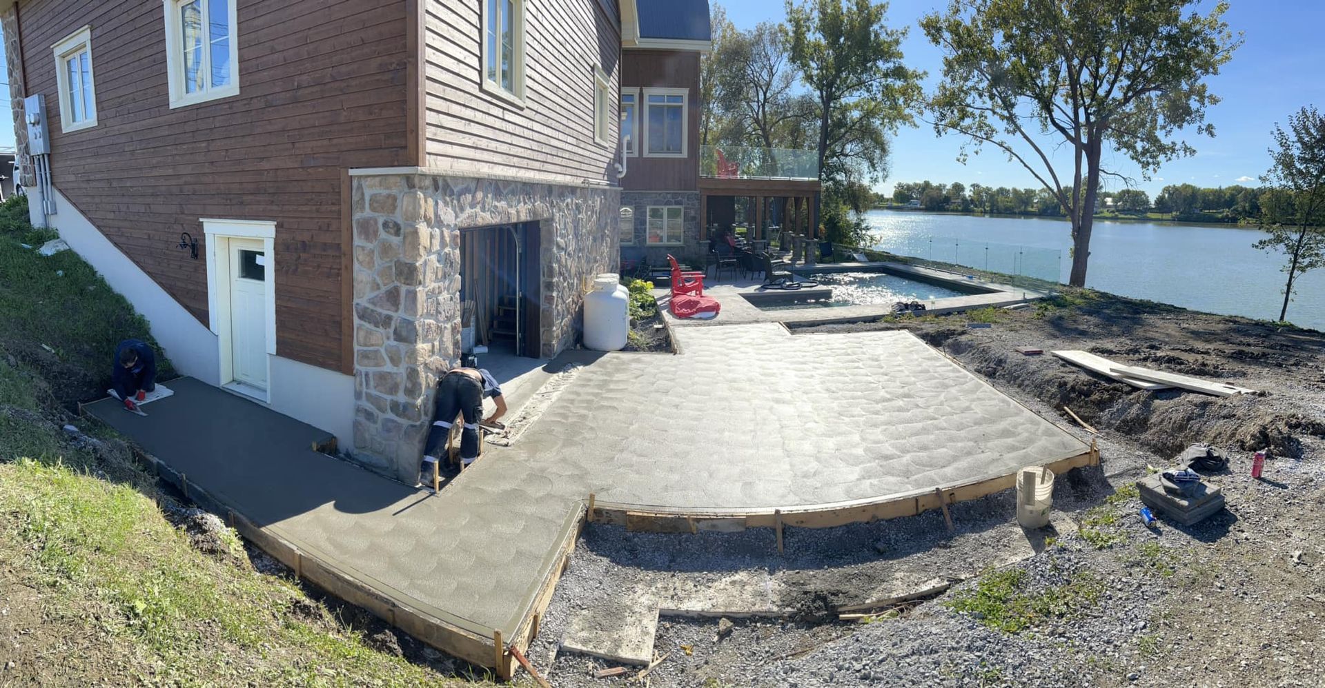 Une grande maison en briques avec un patio devant et un lac en arrière-plan. Coffrage en béton.