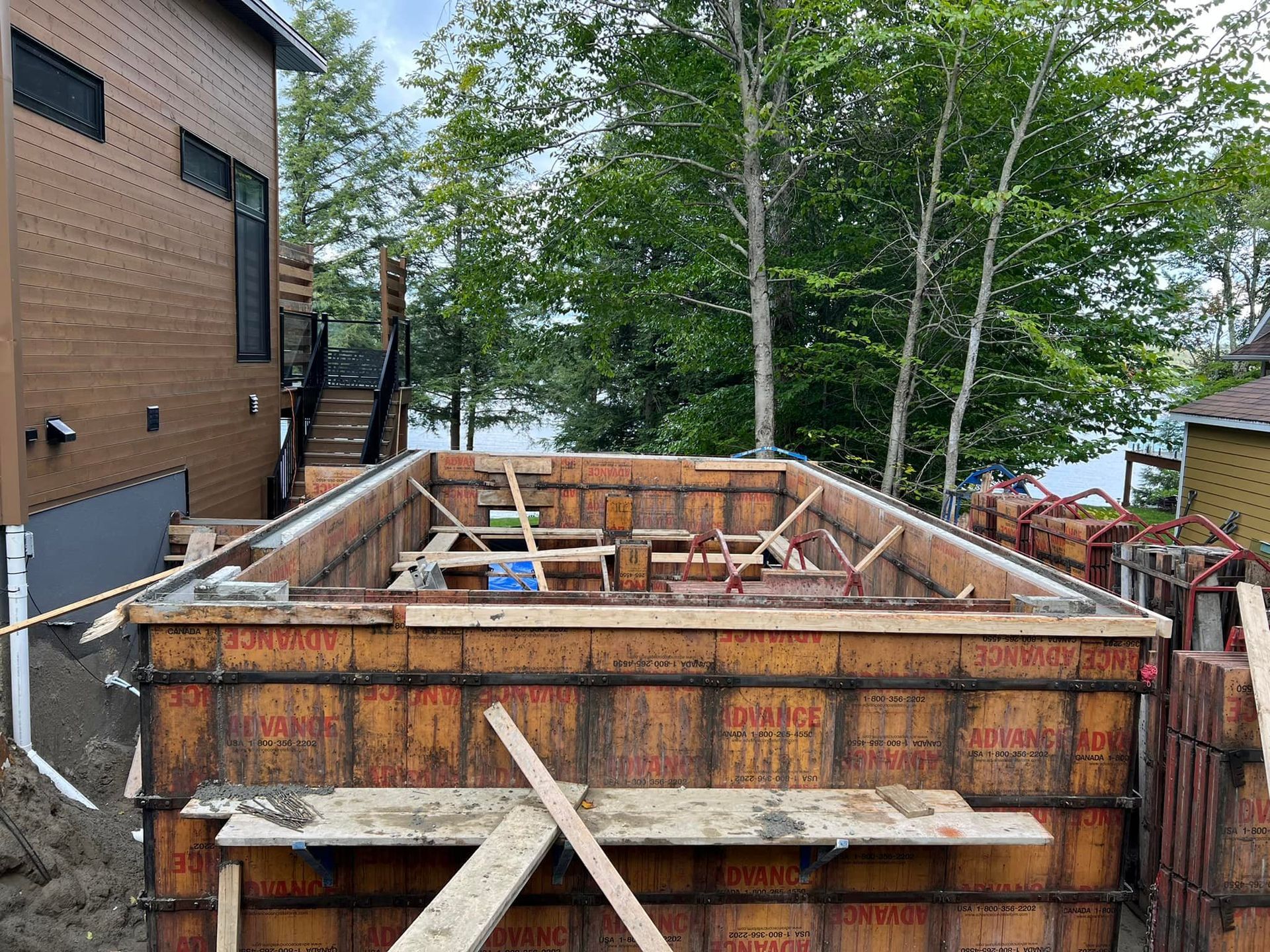 Une grande piscine est en cours de construction devant une maison. Coffrage.