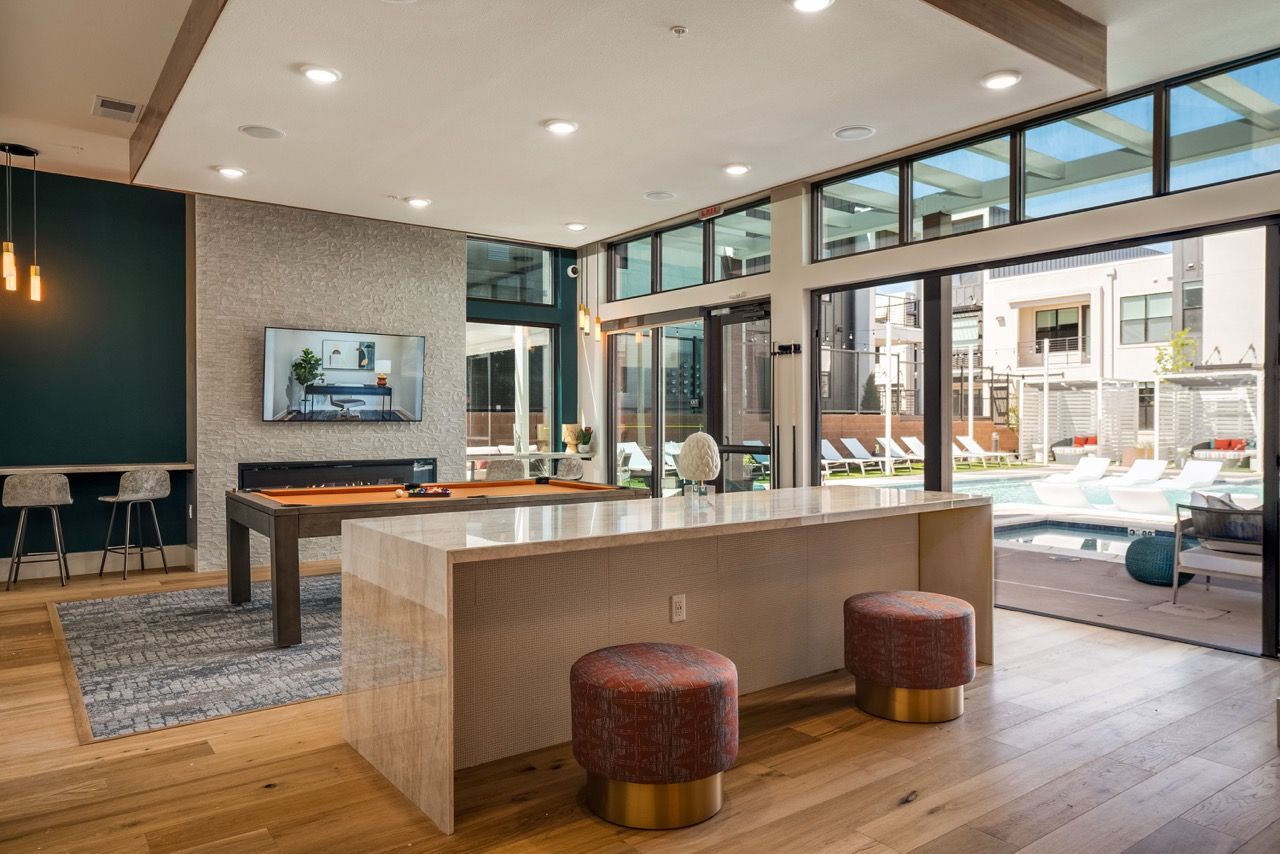 Modern indoor clubhouse lounge with a large island counter and glass walls opening to the outdoor pool.
