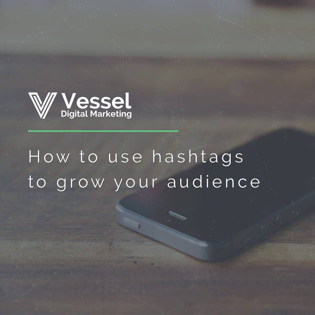 A cell phone is sitting on a wooden table with the words how to use hashtags to grow your audience