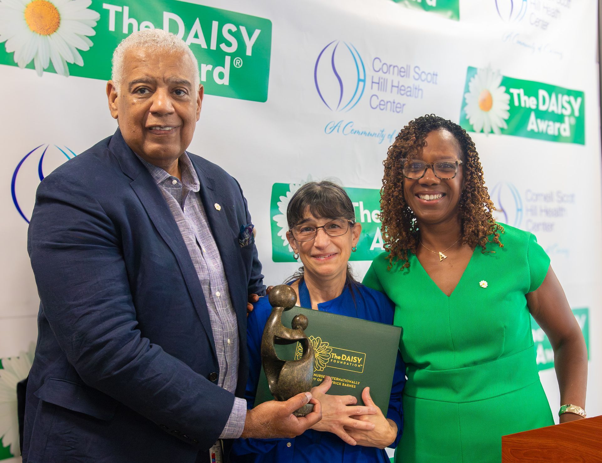 Three people hold a Daisy Award trophy and certificate at a hospital recognition event.