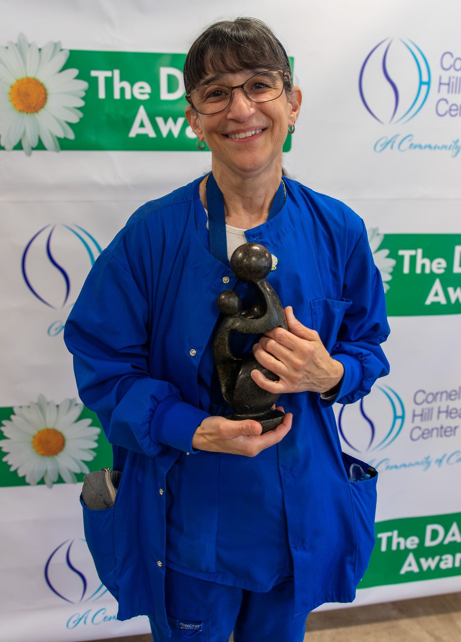 Woman in blue holds a trophy at an award ceremony backdrop.