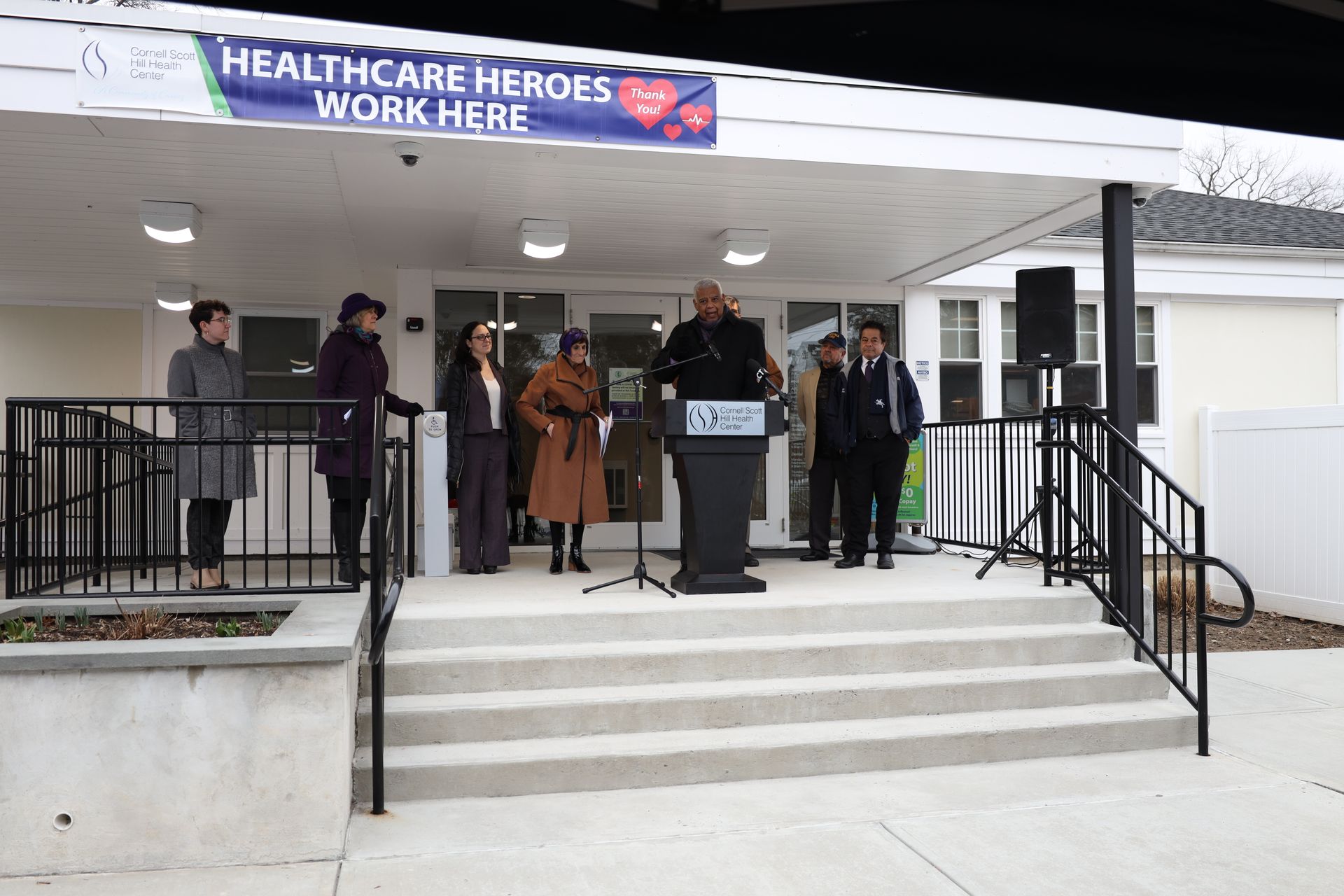 People standing on a front porch with a “Healthcare Heroes Work Here” banner above the entrance