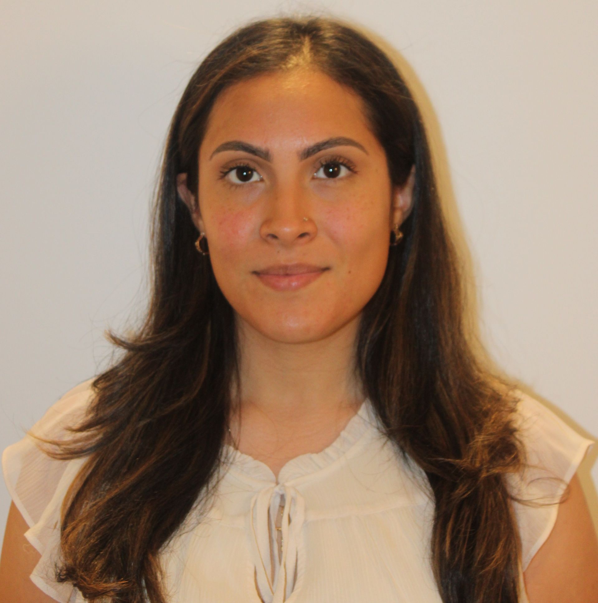 Portrait of a woman with long dark hair, wearing a white blouse, against a plain beige background