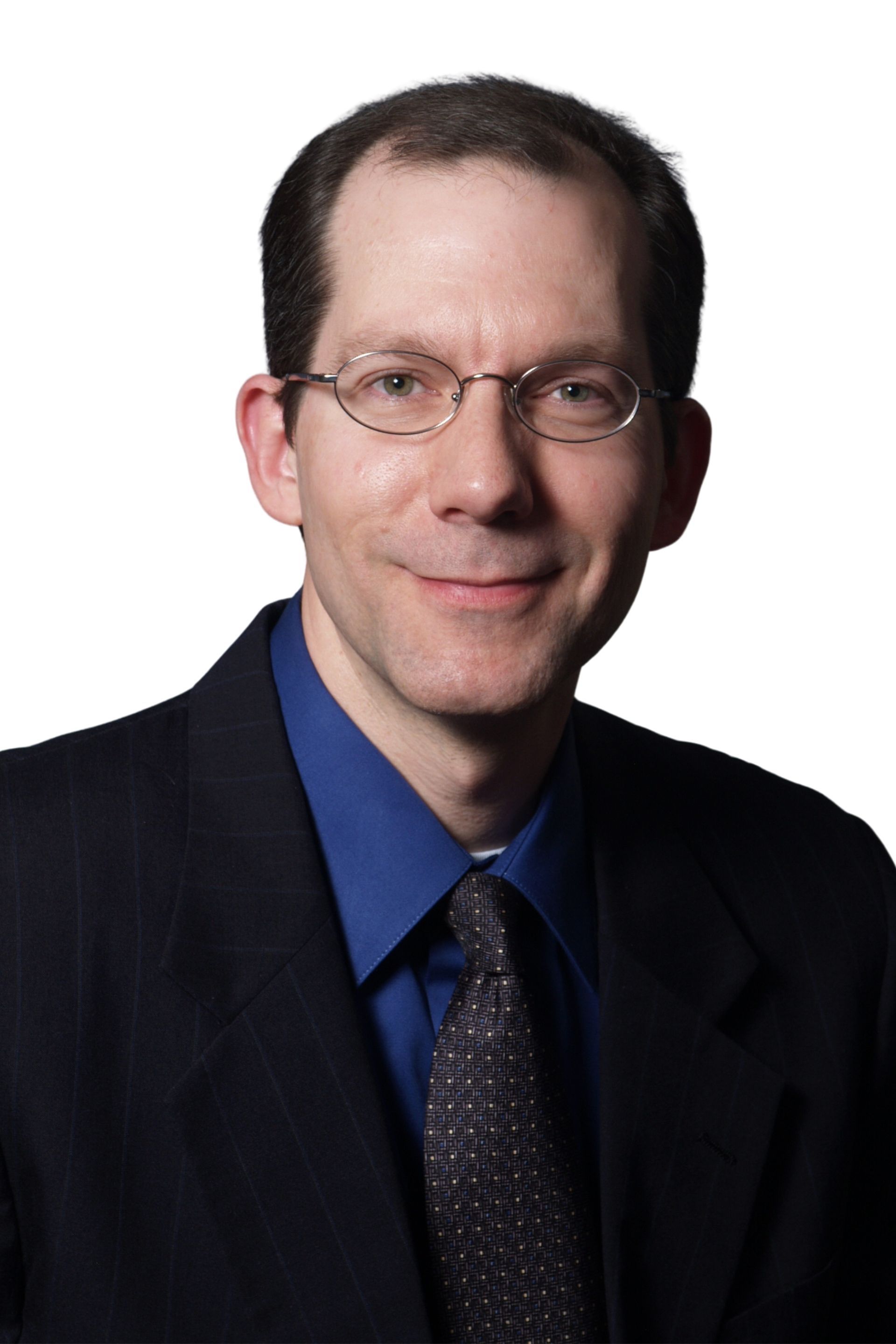 Portrait of a man in a dark suit, blue shirt, and glasses against a white background