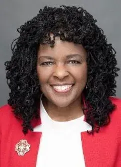 Smiling woman in a red blazer and white top against a gray background