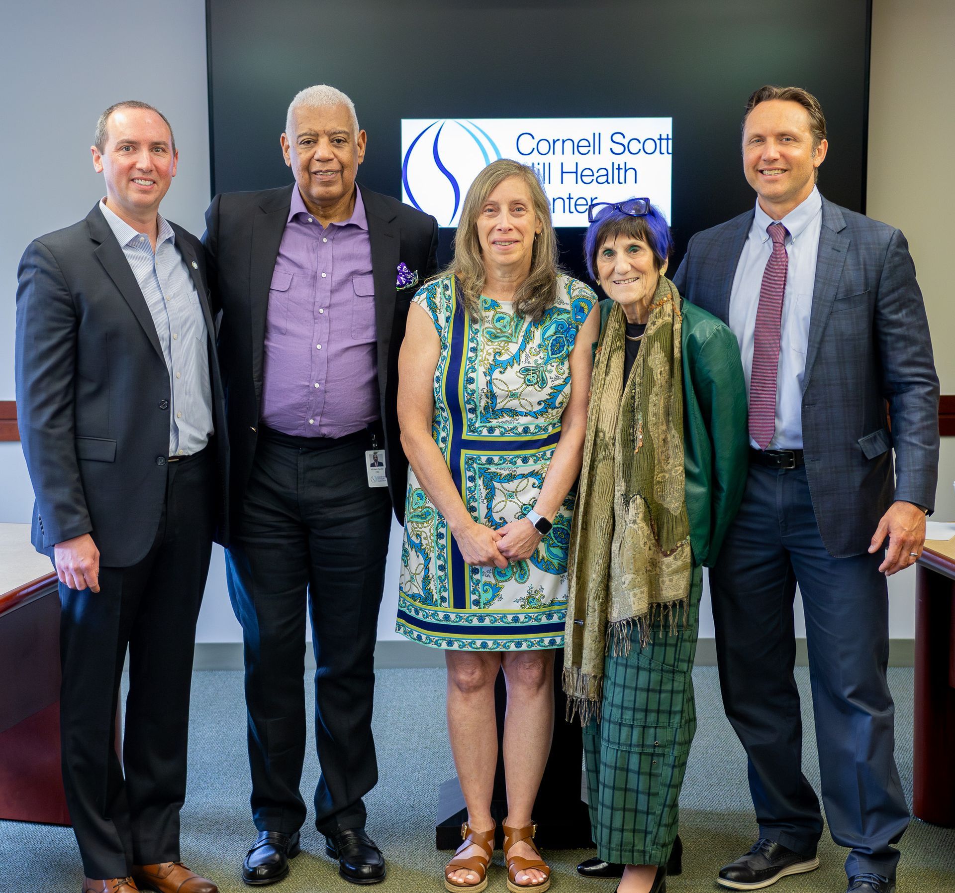 Five people standing in front of a Cormel South Health sign, smiling at an indoor event.